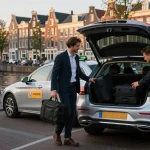 Taxirit in Amsterdam met een professionele chauffeur die bagage laadt bij Schiphol, met de nadruk op comfort en luxe.