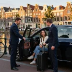 Taxi Amsterdam service met Mercedes E-Klasse en glimlachende passagiers in een schilderachtige achtergrond.